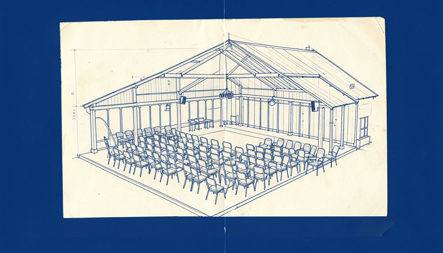 A hand-drawn technical blueprint sketch of a Welsh village hall stage with rows of chairs, rendered in muted navy blue lines